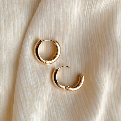 Pair of 16mm chunky gold huggie hoop earrings with a smooth, gold-plated finish, displayed on soft neutral fabric. Classic, minimalist jewelry perfect for everyday wear.