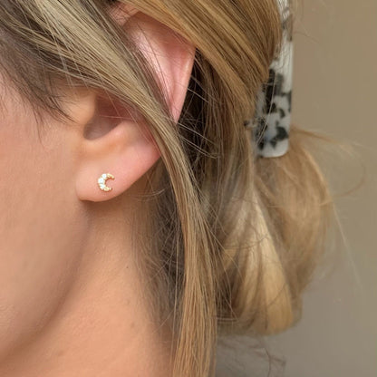 Close-up of a woman wearing a dainty gold crescent moon stud earring with sparkling cubic zirconia stones. Minimalist celestial jewelry, perfect for everyday wear or layering.